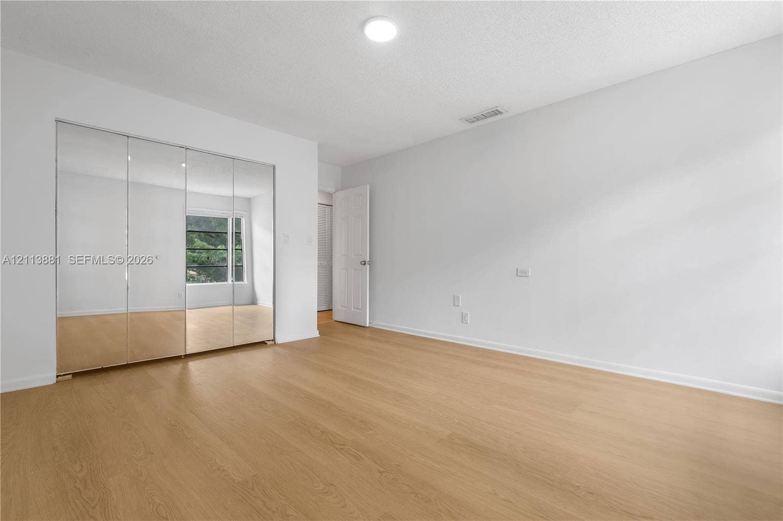 3886 Meadow Lane, #250, Hollywood, FL 33021 Room featuring wood-finish flooring, floor-to-ceiling mirrored sliding closet doors, a multi-panel door, and a single-light fixture
