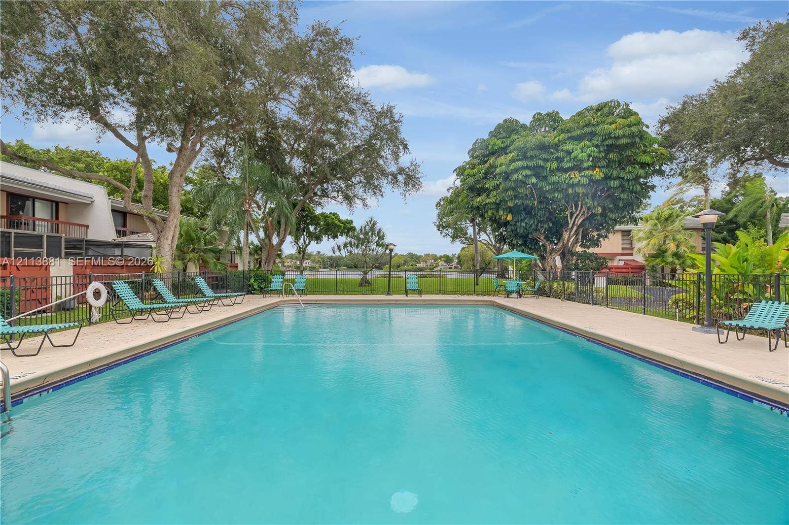 3886 Meadow Lane, #250, Hollywood, FL 33021 Rectangular swimming pool featuring a concrete deck, metal perimeter fencing, and mature landscaping