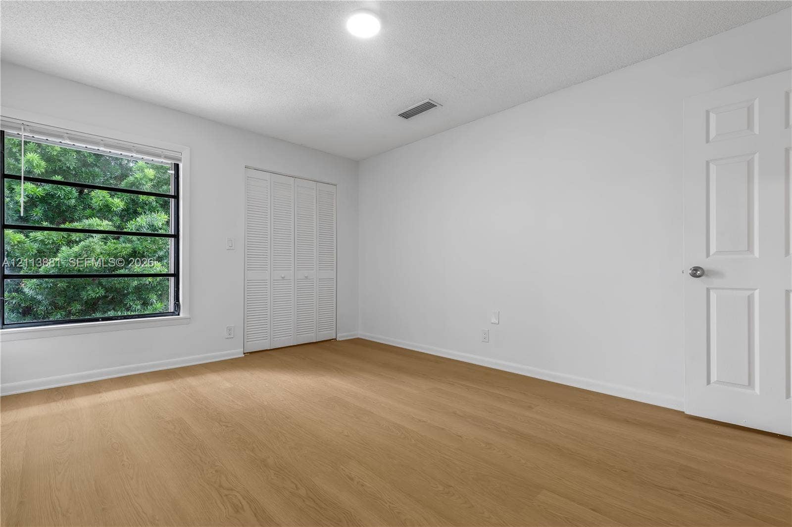 3886 Meadow Lane, #250, Hollywood, FL 33021 Wood-finish flooring, large window with natural scenery, ceiling-mounted light fixture, and white louvered closet doors