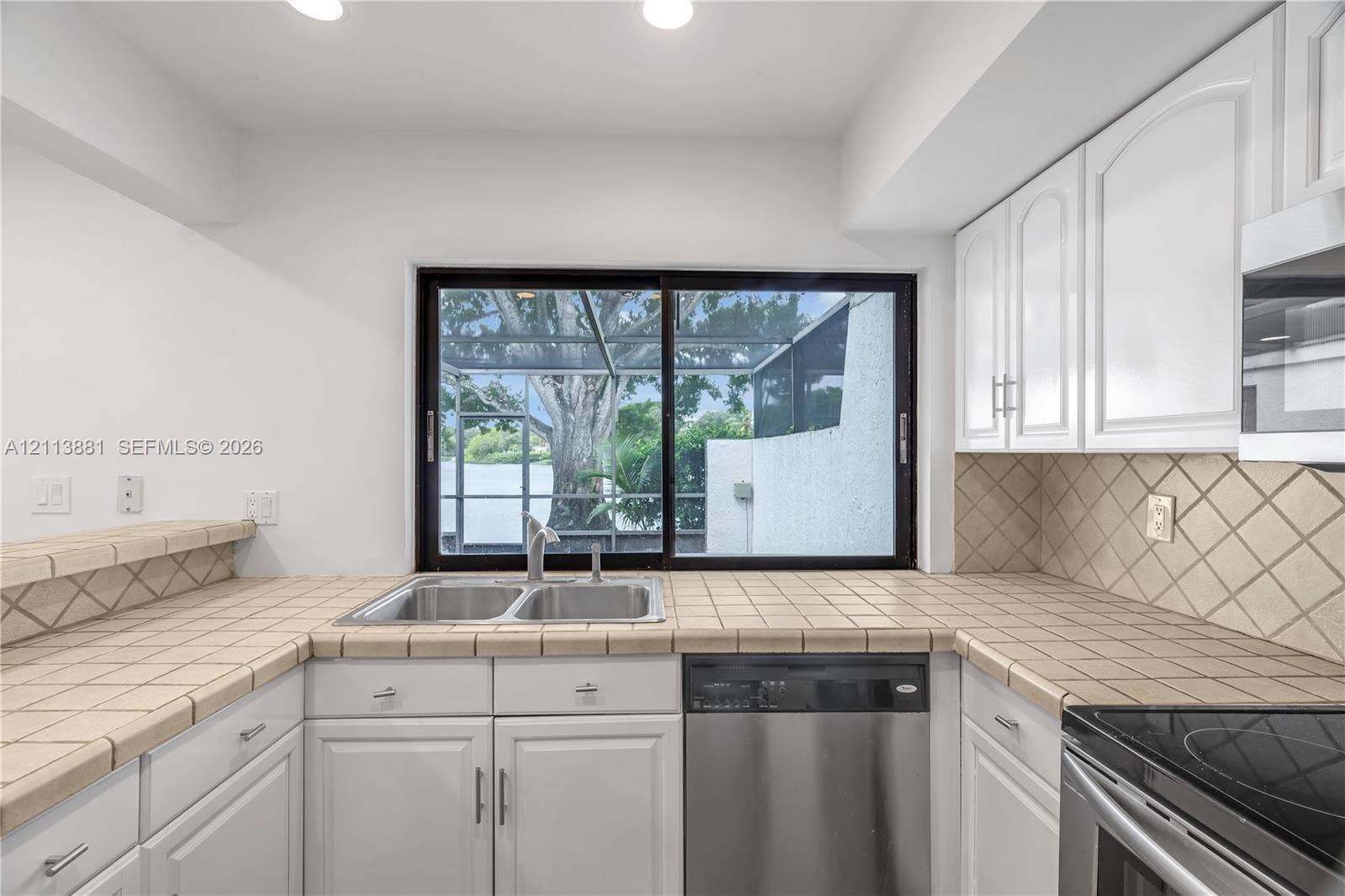 3886 Meadow Lane, #250, Hollywood, FL 33021 Kitchen featuring white cabinetry, tile countertops, diamond-patterned tile backsplash, stainless steel dishwasher, and sliding glass window