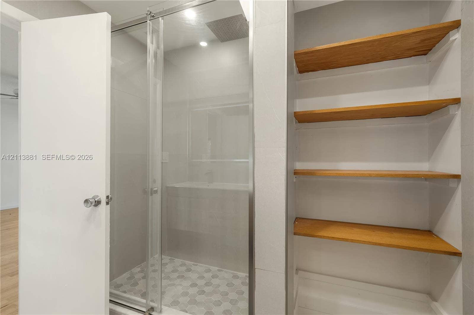 3886 Meadow Lane, #250, Hollywood, FL 33021 Walk-in shower featuring a glass enclosure, oversized rain shower head, hexagonal tile flooring, and integrated wood-finish shelving