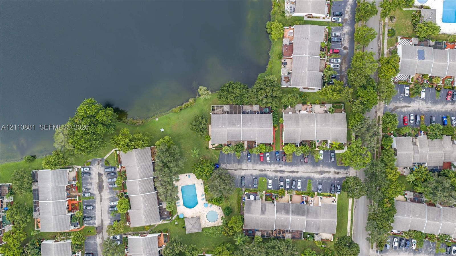 3886 Meadow Lane, #250, Hollywood, FL 33021 Aerial perspective of multi-family residences featuring waterfront positioning, expansive green space, mature trees, and a shared swimming pool