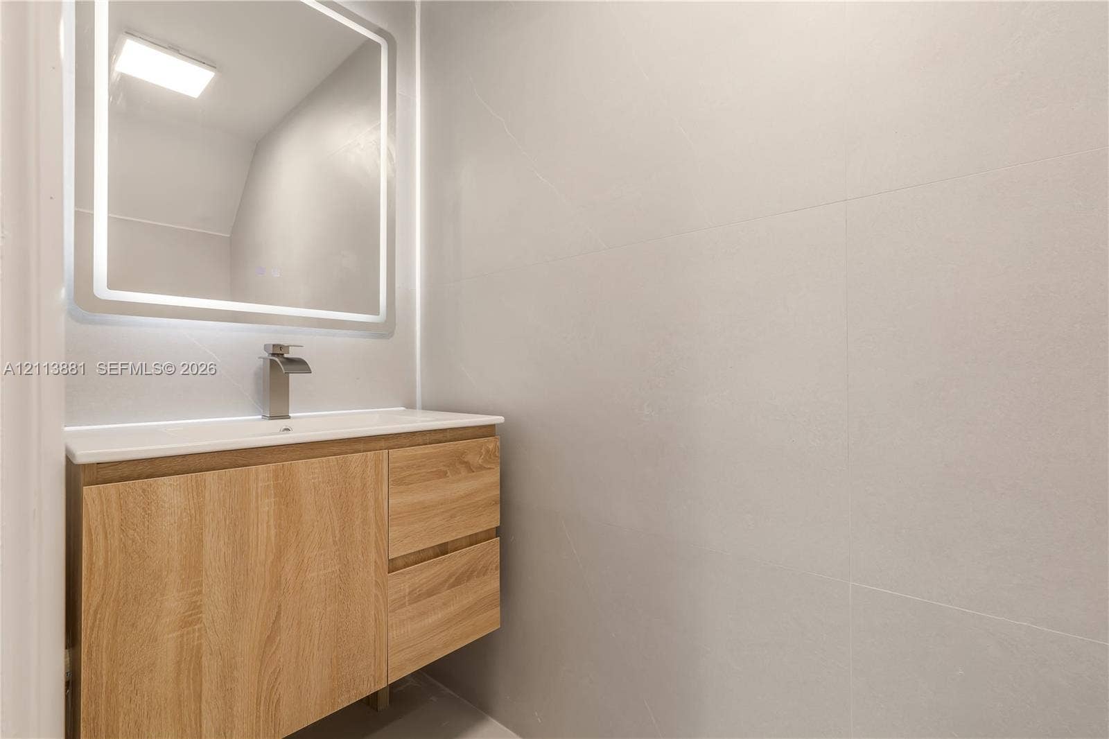 3886 Meadow Lane, #250, Hollywood, FL 33021 Floating wood-finish vanity with a rectangular sink, brushed nickel faucet, wall-mounted LED-backlit mirror, and large-format neutral wall tile