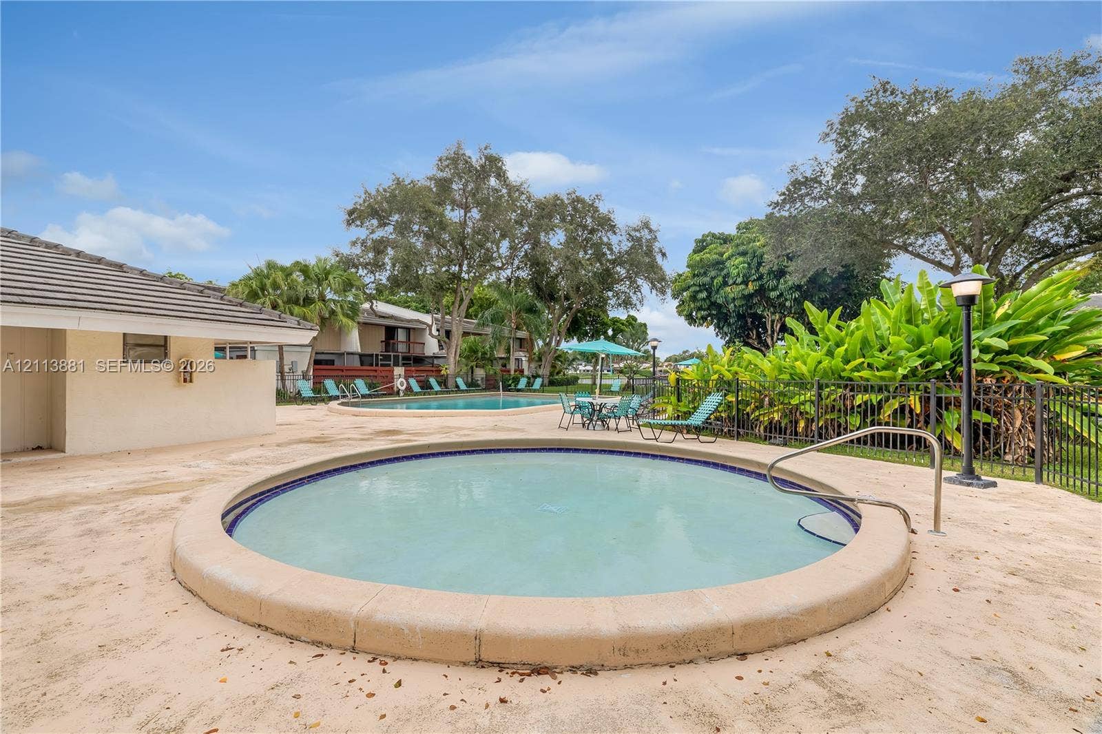 3886 Meadow Lane, #250, Hollywood, FL 33021 Circular spa featuring a concrete surround, metal handrail, and tile inlay, complemented by a secondary swimming pool, expansive concrete decking, and mature landscaping