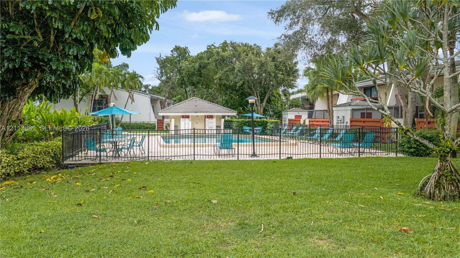 3886 Meadow Lane, #250, Hollywood, FL 33021 Outdoor recreation area featuring an in-ground swimming pool, a covered pool house, perimeter metal fencing, and landscaped grounds