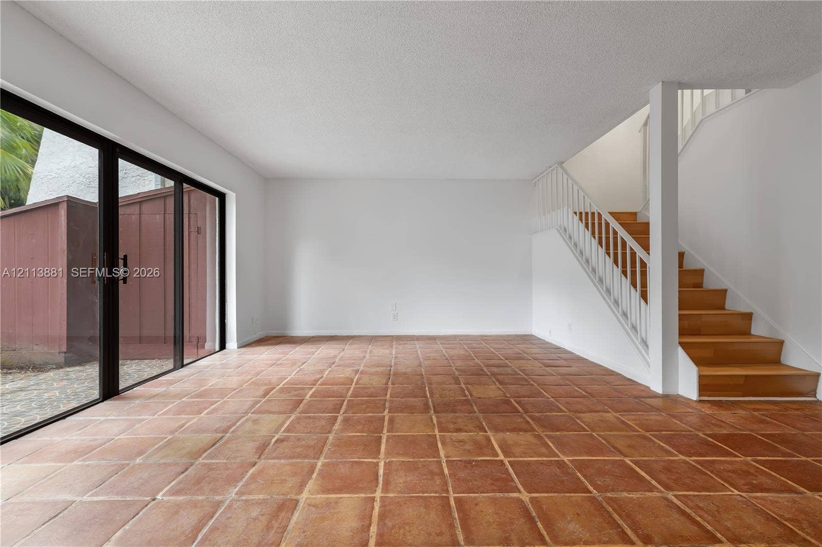 3886 Meadow Lane, #250, Hollywood, FL 33021 Living area featuring terracotta tile flooring, floor-to-ceiling sliding glass doors, and a staircase with wood-finish treads and white vertical railings