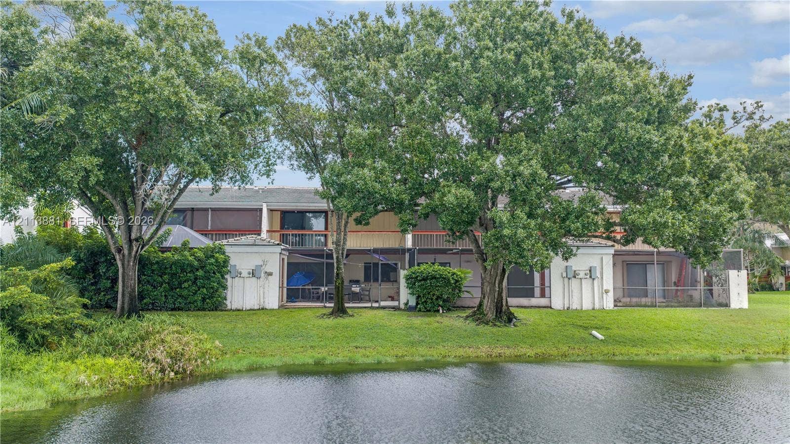 3886 Meadow Lane, #250, Hollywood, FL 33021 Exterior featuring waterfront positioning, multiple screened-in ground-level lanais, second-story balconies, and mature canopy trees