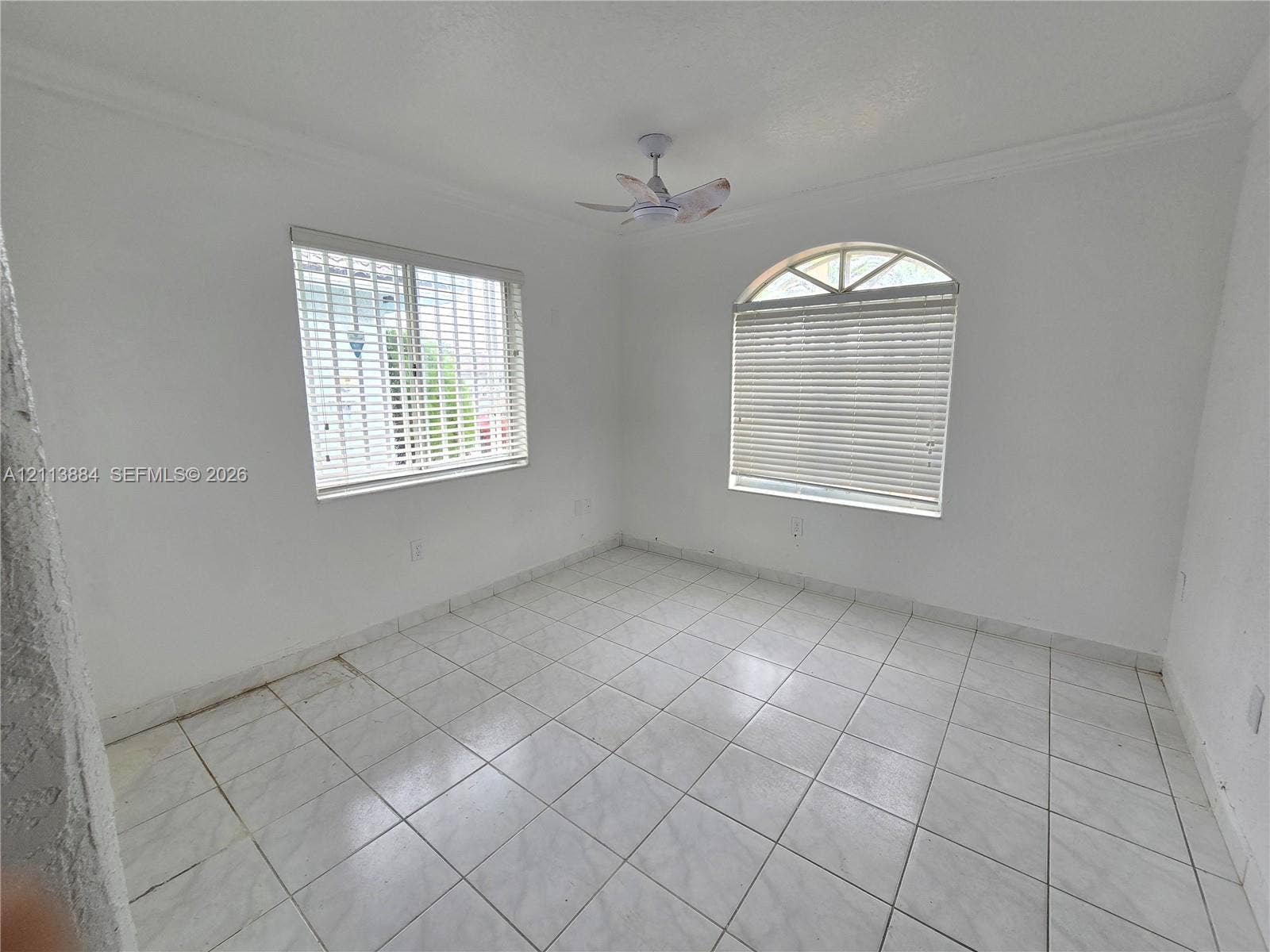 7456 W 34th Court, Hialeah, FL 33018 Room featuring white ceramic tile flooring, an arched window, a ceiling fan, and crisp crown molding