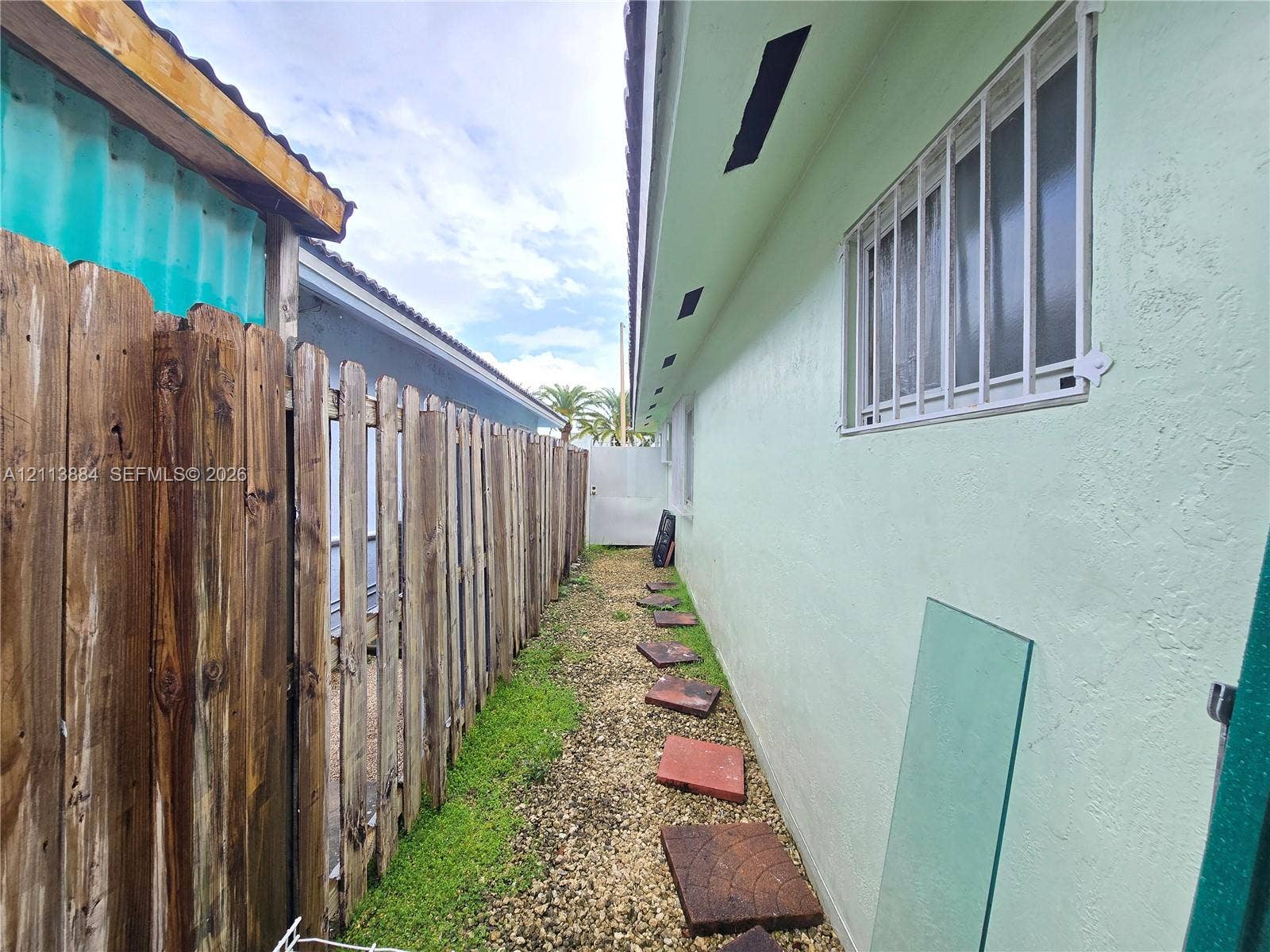 7456 W 34th Court, Hialeah, FL 33018 Side exterior featuring a stucco facade, metal security window bars, a wood picket fence, and stone paver walkway