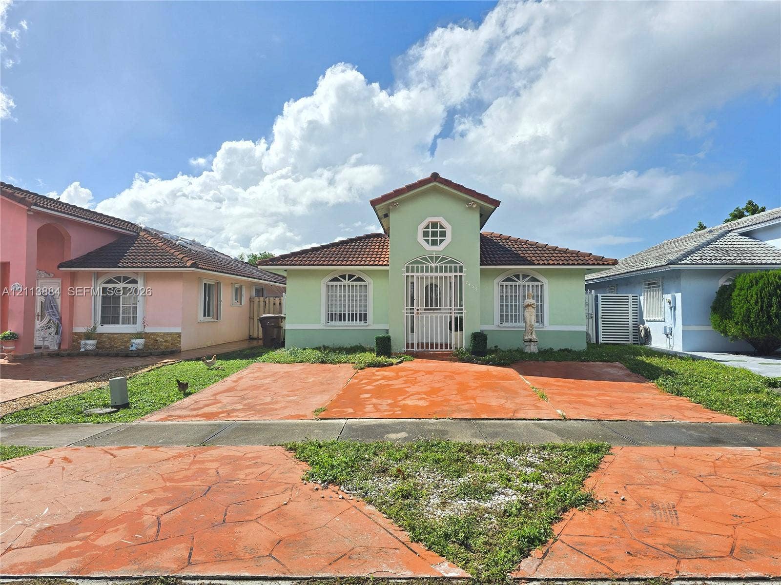 7456 W 34th Court, Hialeah, FL 33018 Single-story residence featuring a tile roof, arched window detailing, an octagonal accent window, and an integrated metal security gate entry
