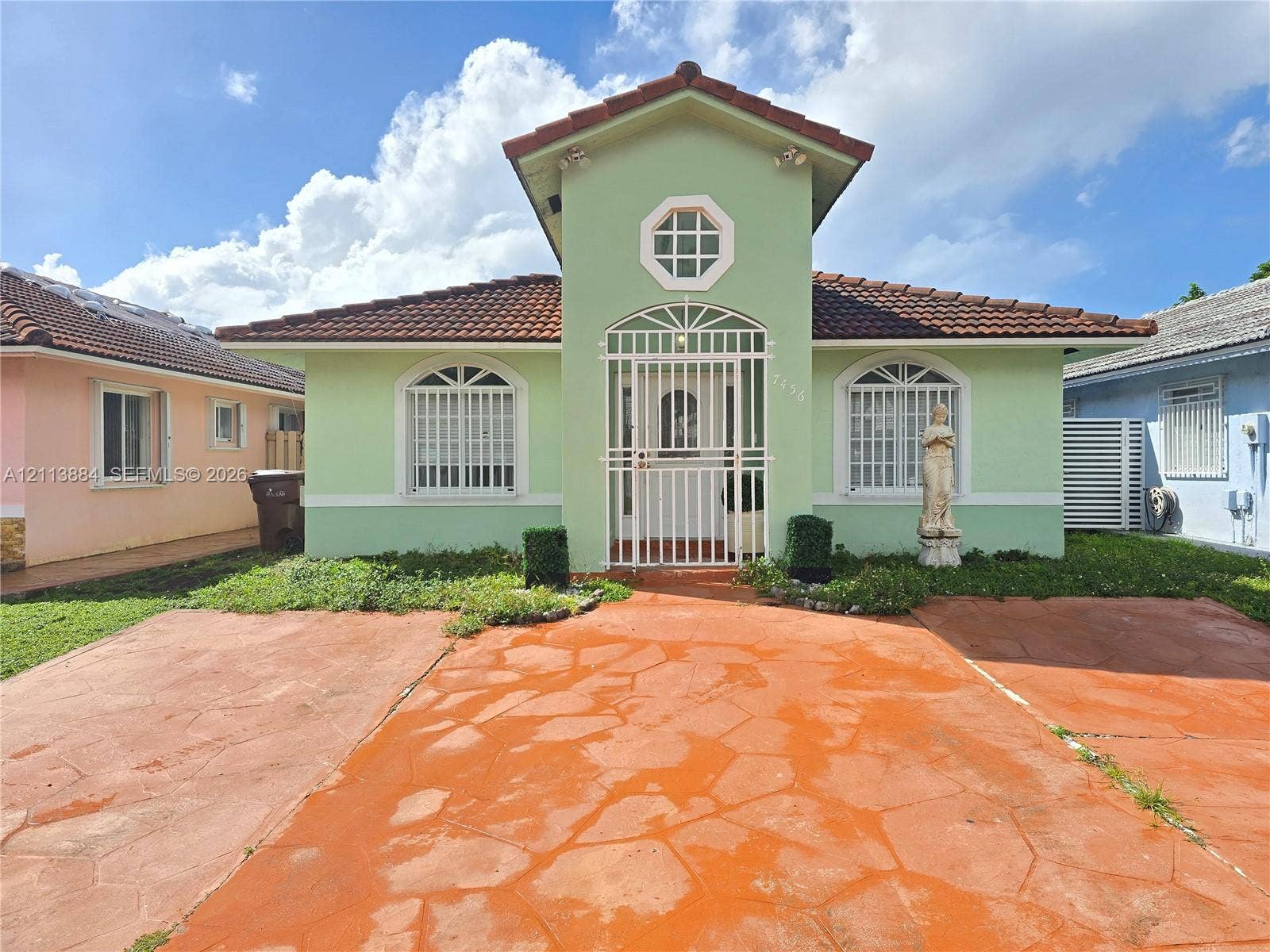 7456 W 34th Court, Hialeah, FL 33018 Stucco exterior with a central gable, tiled roof, arched windows featuring security grilles, and a stained concrete driveway