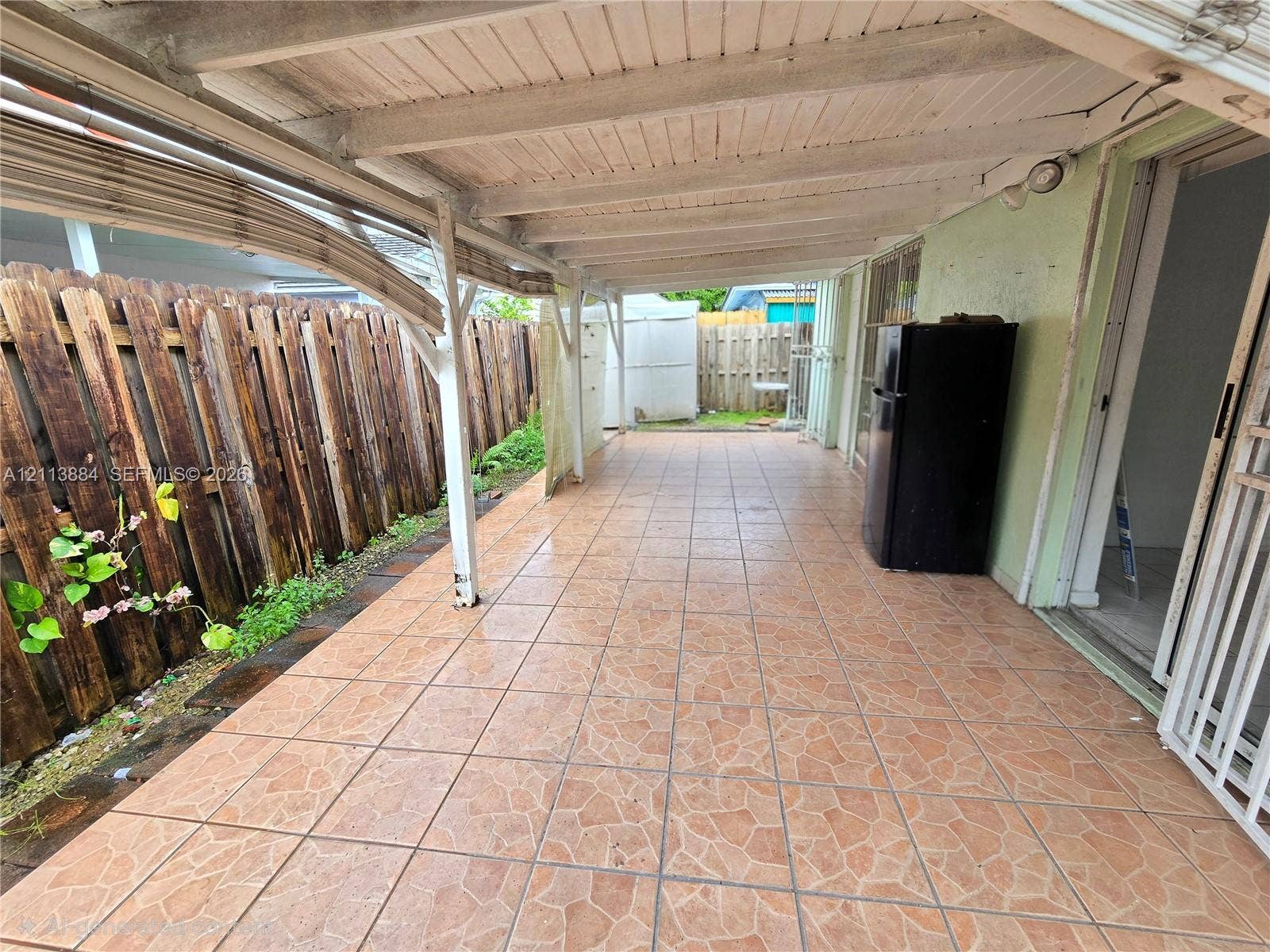 7456 W 34th Court, Hialeah, FL 33018 Covered outdoor patio featuring tile flooring, a painted wooden ceiling, and vertical wood-plank perimeter fencing