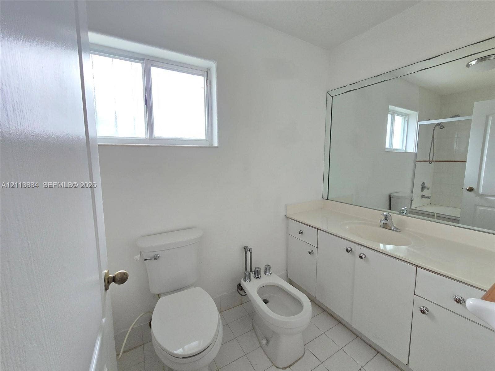 7456 W 34th Court, Hialeah, FL 33018 Bathroom featuring white cabinetry, integrated vanity countertop with sink, wall-spanning mirror, bidet, and tile flooring
