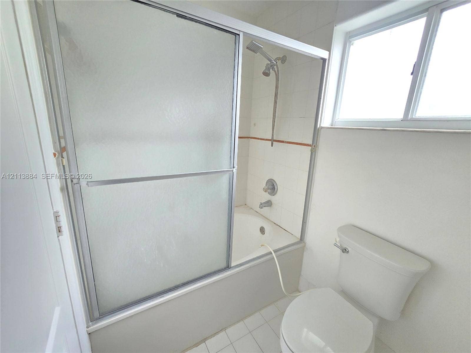 7456 W 34th Court, Hialeah, FL 33018 Bathtub and shower combination featuring sliding textured glass doors, tiled surround, wall-mounted shower head, and white floor tiling