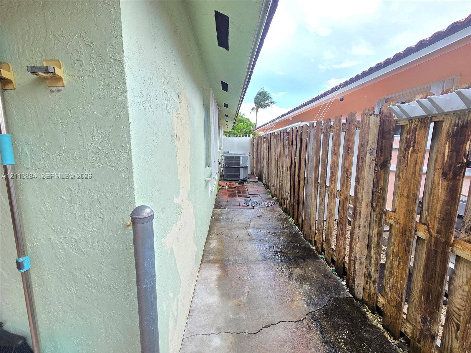 7456 W 34th Court, Hialeah, FL 33018 Side exterior area featuring a concrete pathway, vertical wood privacy fencing, and an external HVAC condenser unit