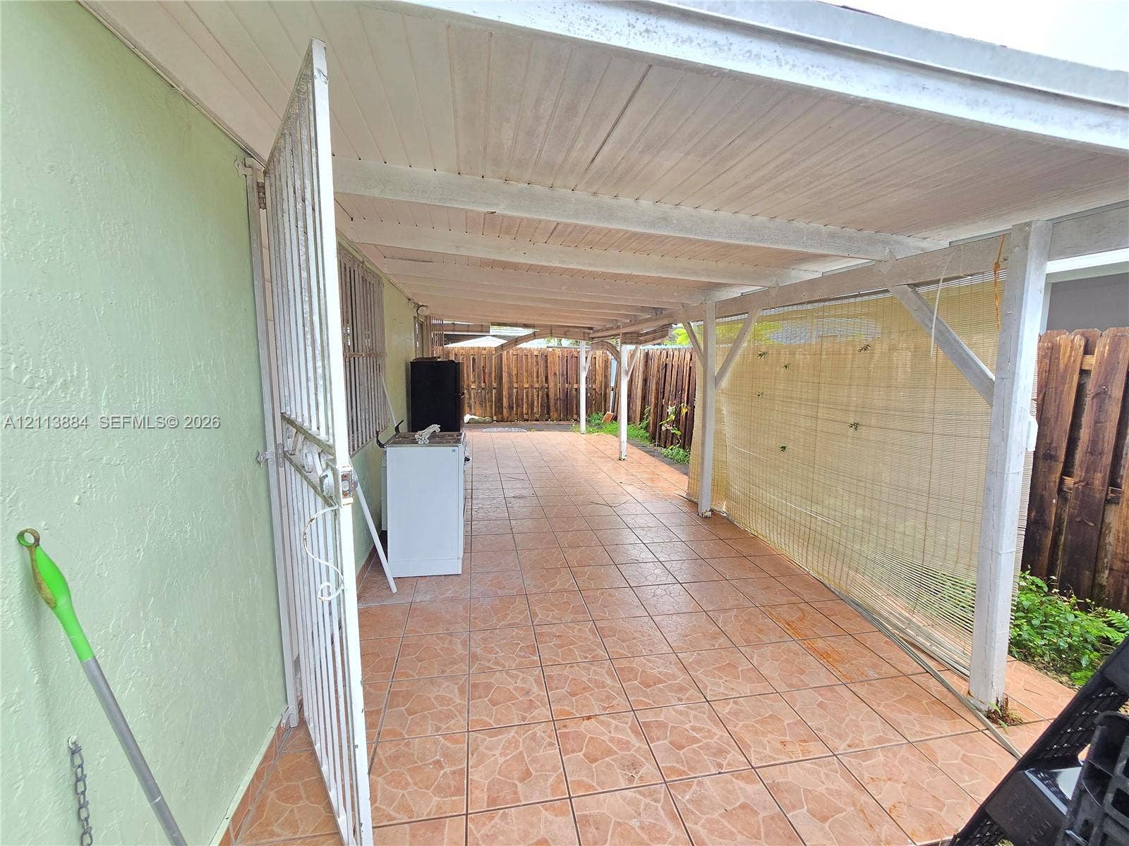 7456 W 34th Court, Hialeah, FL 33018 Covered patio featuring tiled flooring, a wooden support structure, and a perimeter wood-slat fence