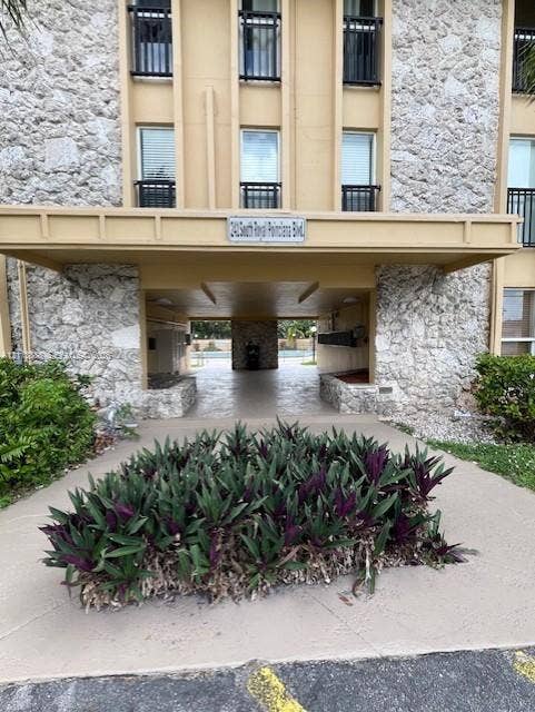 241 S Royal Poinciana Boulevard, #102, Miami Springs, Miami Springs, FL 33166 Building exterior featuring stone masonry cladding, a covered porte-cochre, and a landscaped garden bed