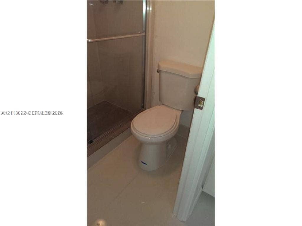 401 Golden Isles Drive, #509, Hallandale Beach, FL 33009 Enclosed shower with glass sliding doors and tile flooring, paired with a standard-profile toilet