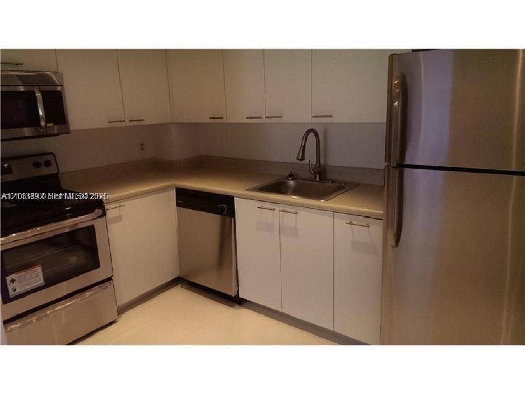 401 Golden Isles Drive, #509, Hallandale Beach, FL 33009 Kitchen featuring white cabinetry, stainless steel appliances, a pull-down faucet, and neutral countertops