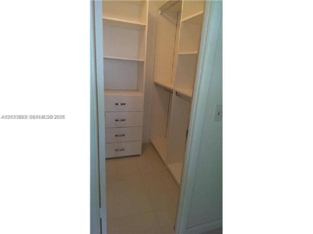 401 Golden Isles Drive, #509, Hallandale Beach, FL 33009 Walk-in closet featuring white built-in shelving, four integrated storage drawers with metal pulls, and hanging rods