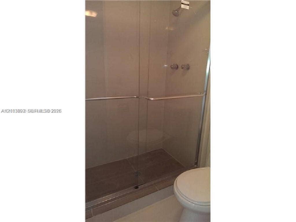 401 Golden Isles Drive, #509, Hallandale Beach, FL 33009 Walk-in shower featuring a glass-panel enclosure, metallic hardware, and neutral-toned wall tiling
