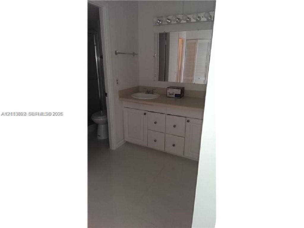 401 Golden Isles Drive, #509, Hallandale Beach, FL 33009 Bathroom vanity featuring solid-surface countertop with integrated oval sink, white cabinetry with hardware pulls, and wall-mounted light fixture above a rectangular mirror