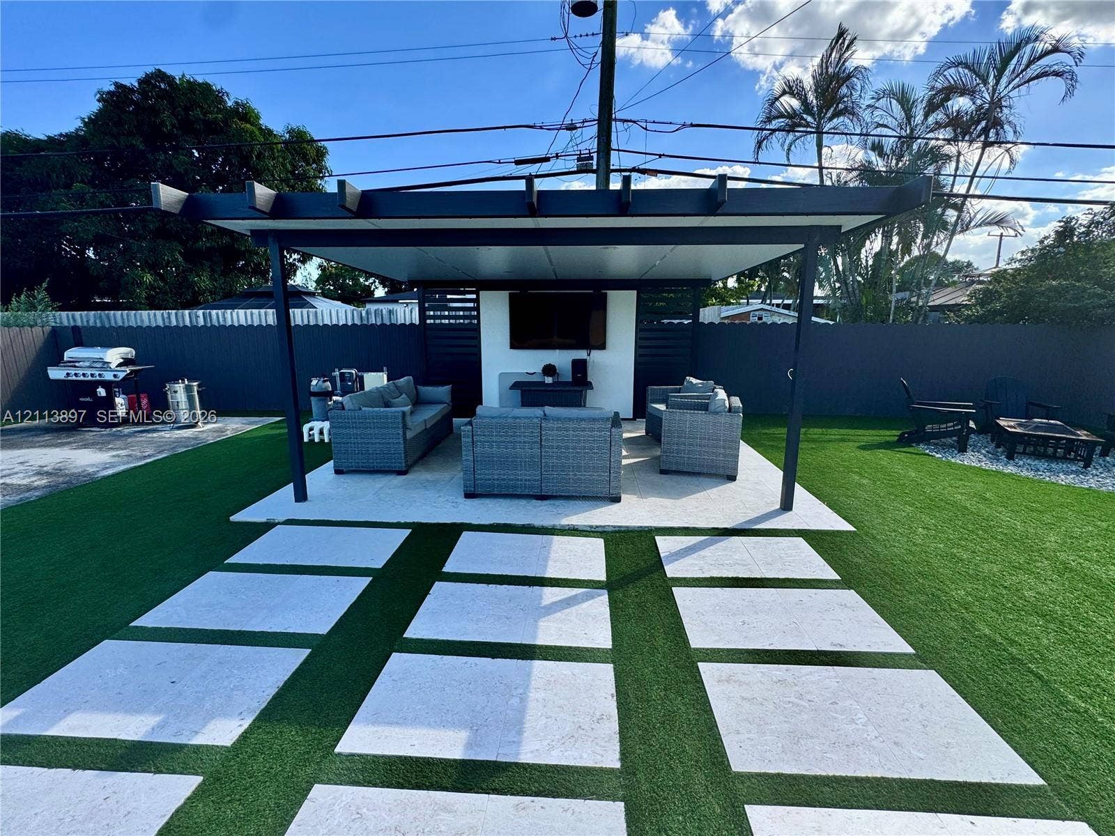 520 E 58th Street, Hialeah, FL 33013 Outdoor covered pavilion with a solid roof structure, concrete paver pathway, synthetic turf lawn, and perimeter privacy fencing