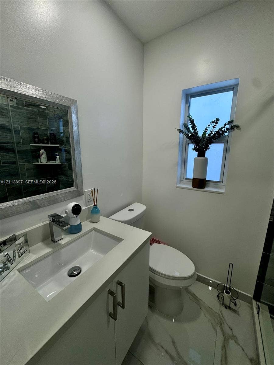 520 E 58th Street, Hialeah, FL 33013 Bathroom featuring a vanity with a white rectangular sink and countertop, framed mirror, stone-finish floor tiling, and a vertical window