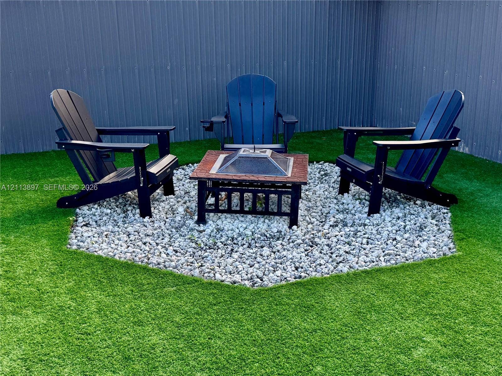 520 E 58th Street, Hialeah, FL 33013 Outdoor area featuring synthetic turf, a hexagonal gravel patio, and corrugated metal fencing