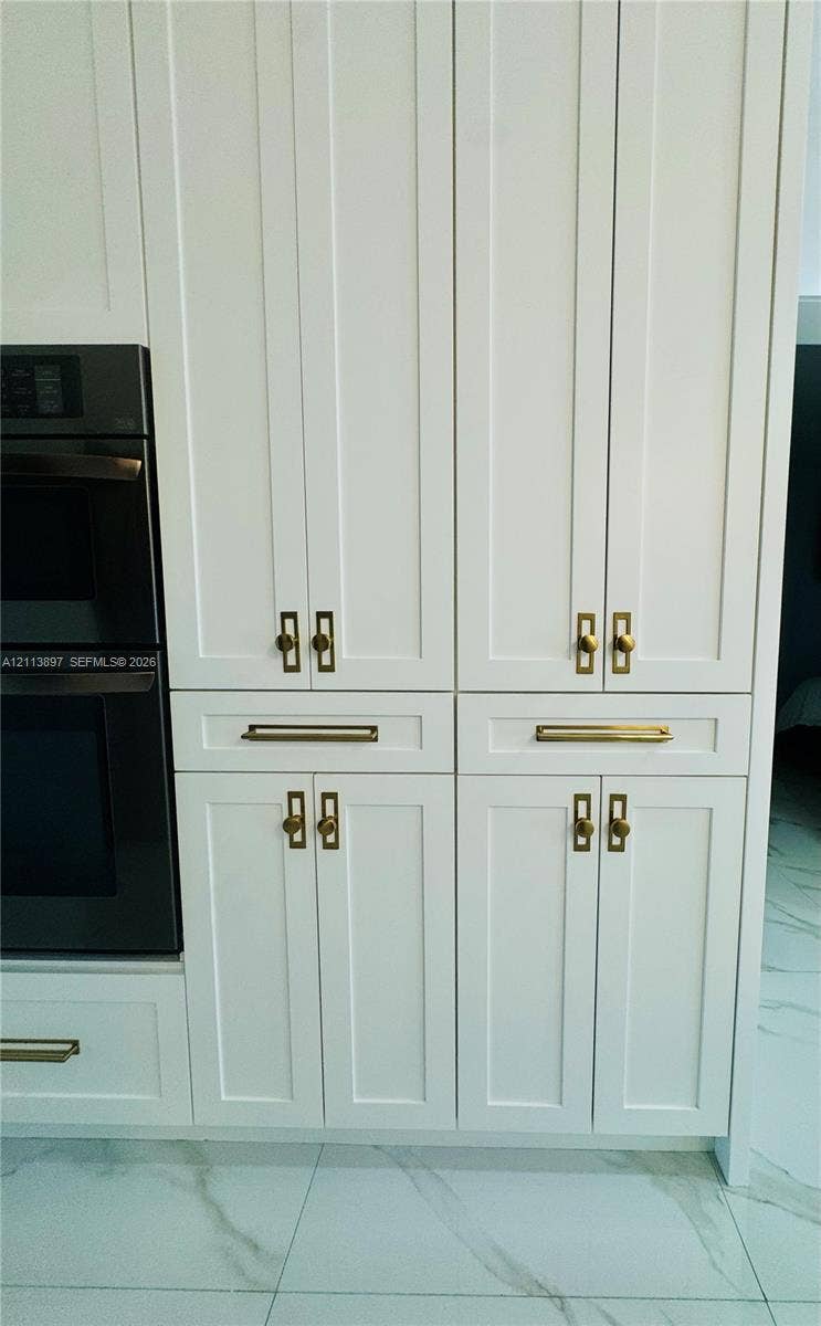 520 E 58th Street, Hialeah, FL 33013 White shaker-style cabinetry with recessed panels, brushed brass hardware, and a built-in double wall oven, set against large-format rectified tile flooring
