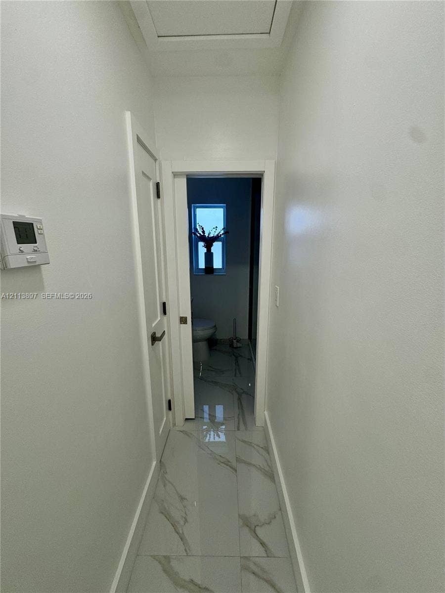 520 E 58th Street, Hialeah, FL 33013 Hallway featuring large-format porcelain tile flooring with veining, a solid-core door with matte black hardware, and a programmable wall-mounted thermostat