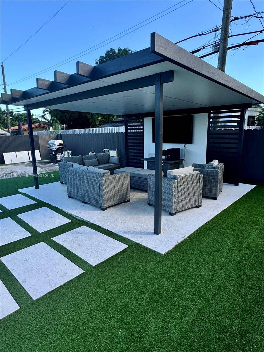520 E 58th Street, Hialeah, FL 33013 Covered outdoor pavilion featuring a flat roof structure, built-in slatted privacy screening, integrated lighting, stone-tiled flooring, and surrounding artificial turf with inset paver pathway