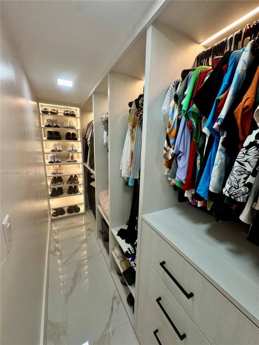 520 E 58th Street, Hialeah, FL 33013 Custom walk-in closet featuring floor-to-ceiling built-in shelving, integrated LED accent lighting, three-drawer cabinetry with matte black hardware, and large-format porcelain tile flooring