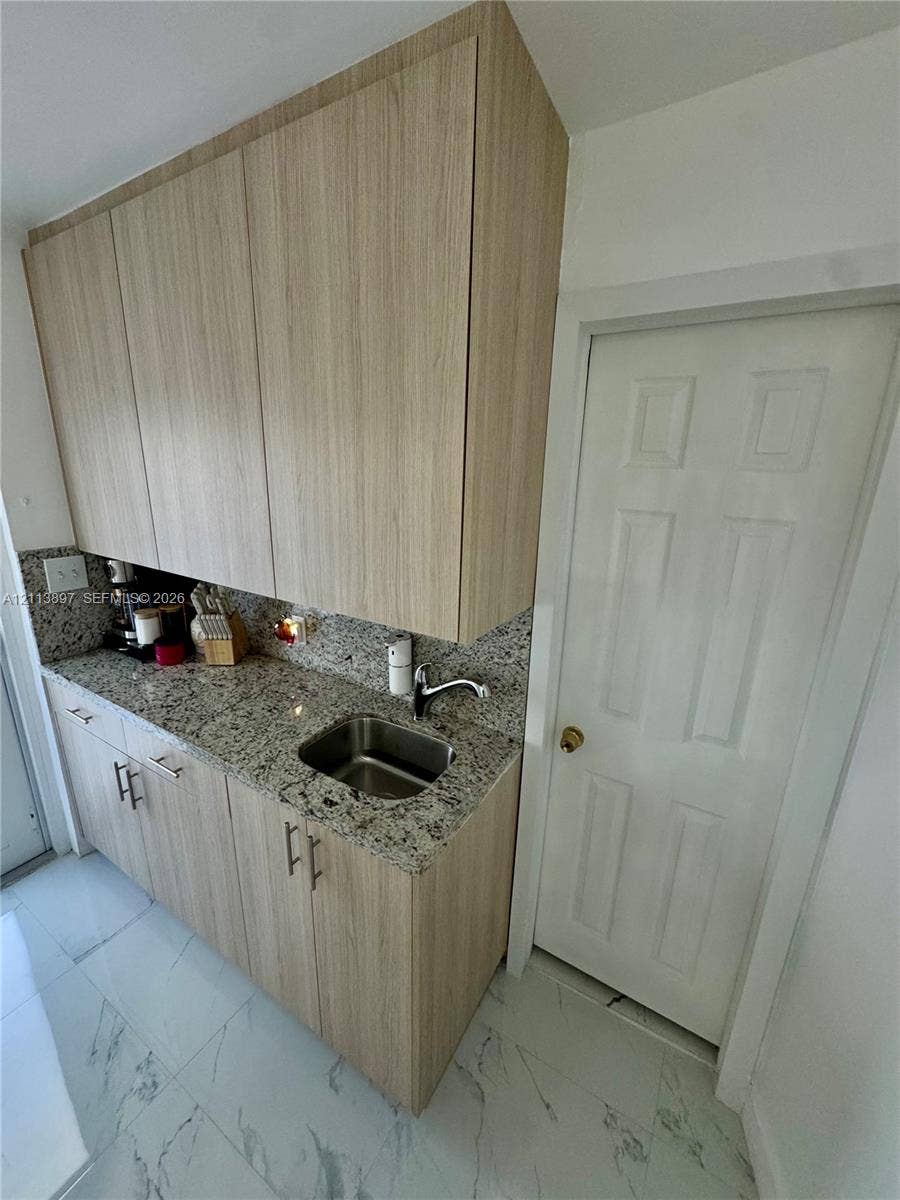 520 E 58th Street, Hialeah, FL 33013 Flat-panel wood-finish cabinetry, speckled stone countertop, stainless steel sink with high-arc faucet, and large-format tile flooring