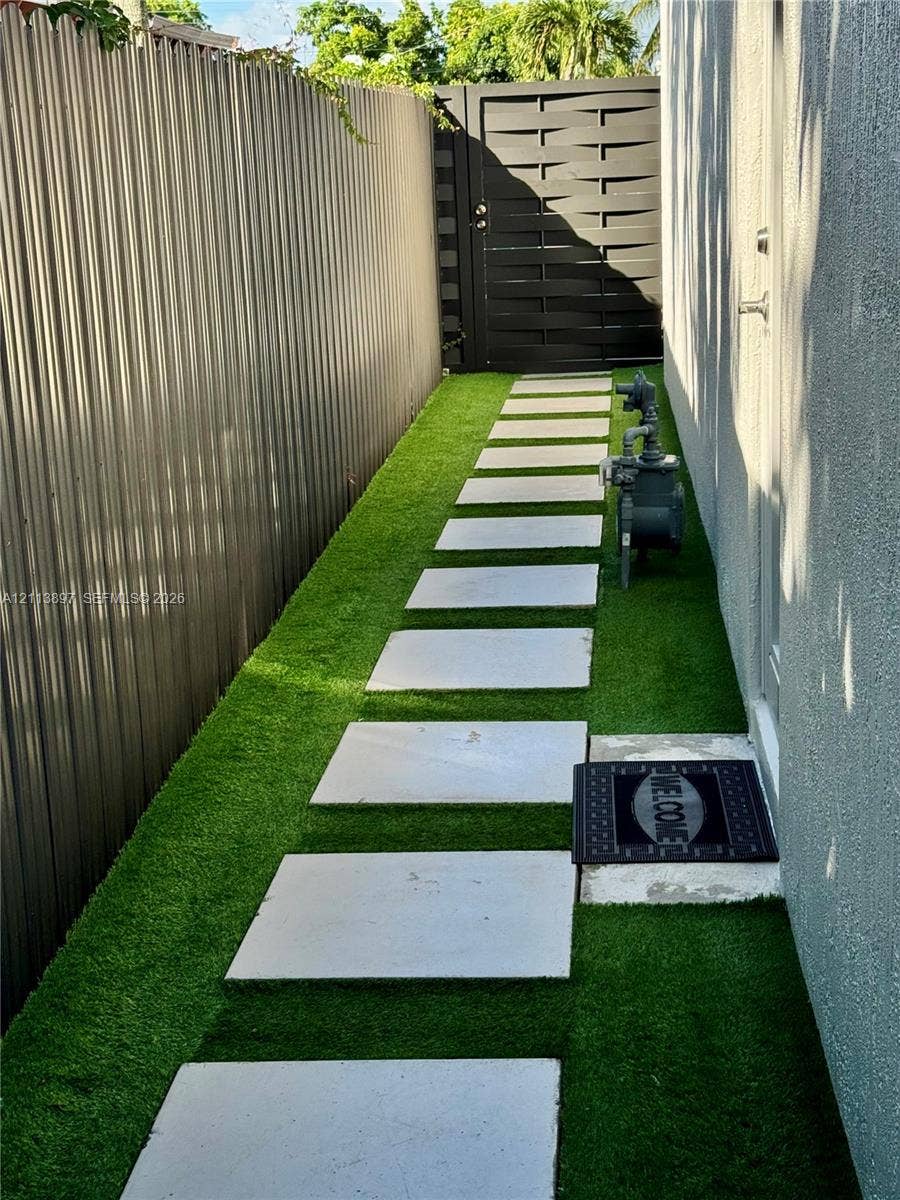 520 E 58th Street, Hialeah, FL 33013 Side yard featuring artificial turf, concrete paver pathway, and metal privacy fencing with a matching pedestrian gate