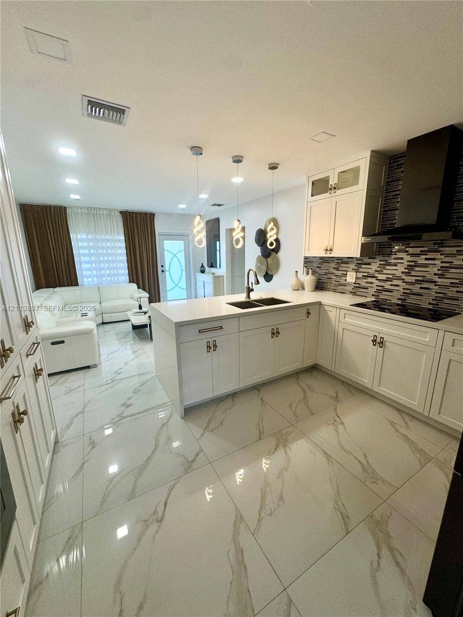 520 E 58th Street, Hialeah, FL 33013 Kitchen featuring white cabinetry, solid-surface countertops, a tiled backsplash, large-format veined flooring, and three pendant light fixtures