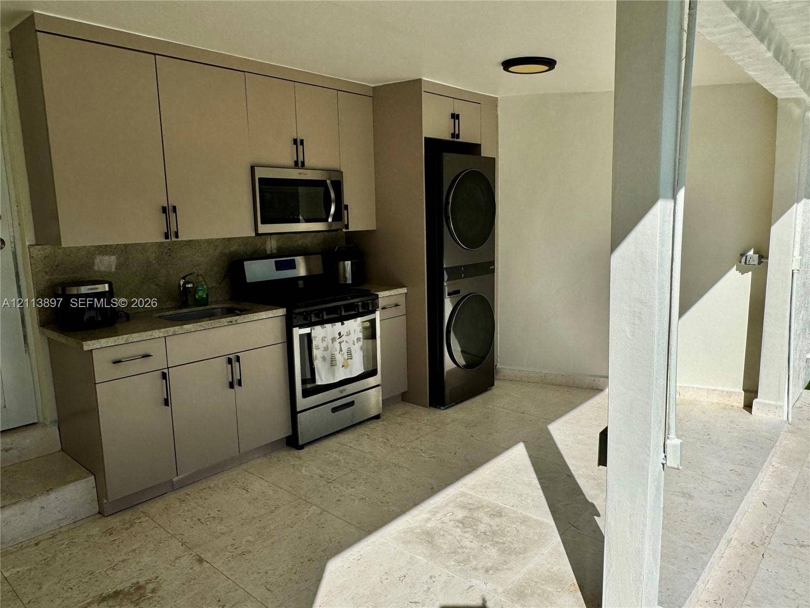 520 E 58th Street, Hialeah, FL 33013 Kitchenette featuring flat-panel cabinetry, stone-finish countertops, stainless steel appliances, and stacked laundry unit, complemented by tile flooring