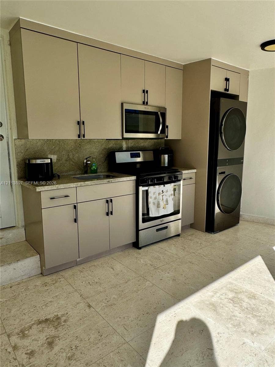 520 E 58th Street, Hialeah, FL 33013 Kitchenette featuring flat-panel cabinetry, stone countertops, stainless steel appliances, and a stacked laundry unit set on stone-finish flooring