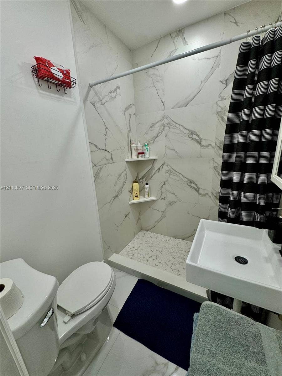 520 E 58th Street, Hialeah, FL 33013 Full-height shower surround with white stone-patterned tile, integrated corner shelving, built-in pebble-finish shower floor, and a wall-mounted rectangular basin