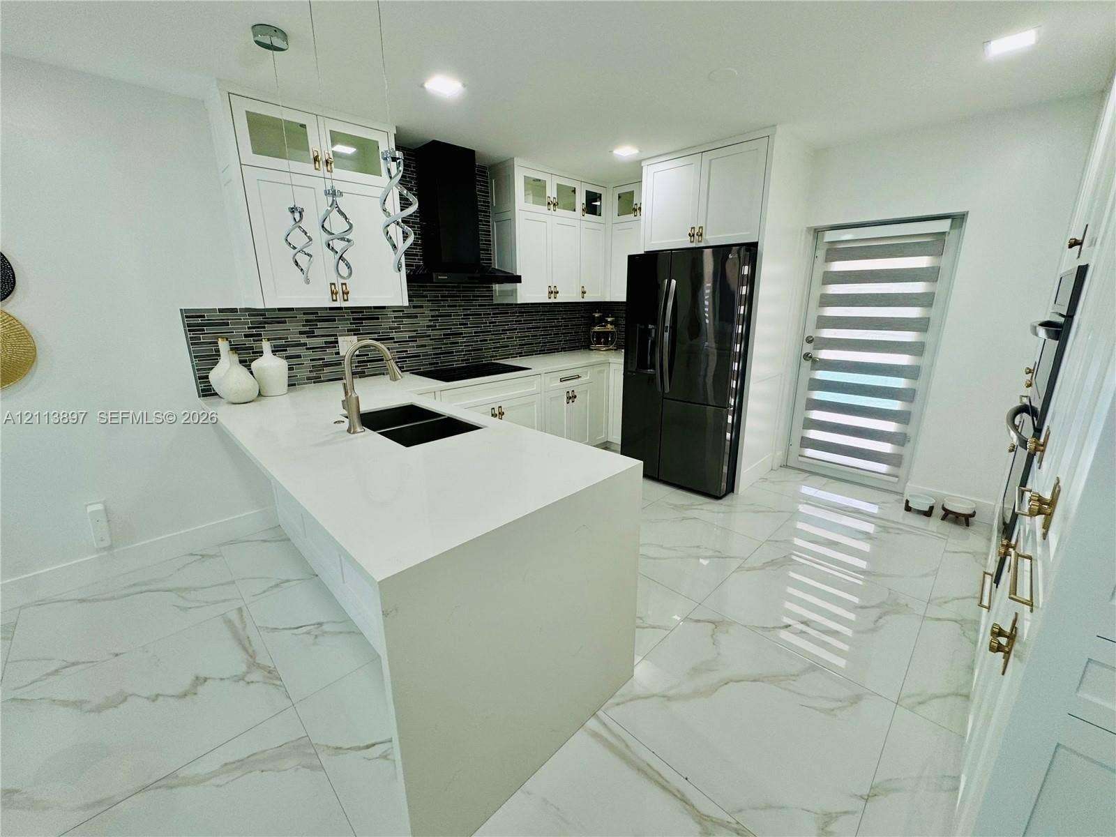 520 E 58th Street, Hialeah, FL 33013 Kitchen featuring white cabinetry with glass-panel accents, stone-composite countertops, a multi-tonal linear tile backsplash, polished stone-finish flooring, and a central island with a double-basin under-mount sink