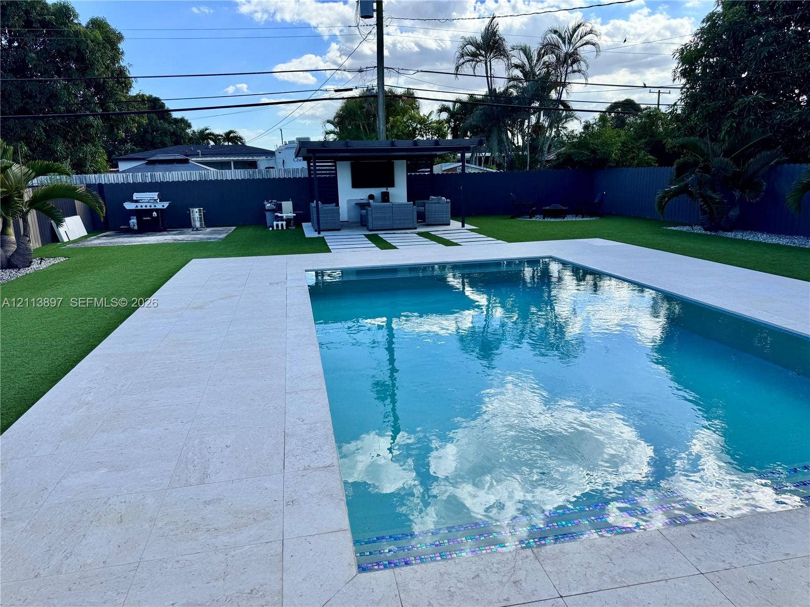 520 E 58th Street, Hialeah, FL 33013 In-ground pool with stone tile surround, covered patio structure, synthetic lawn, and perimeter privacy fencing