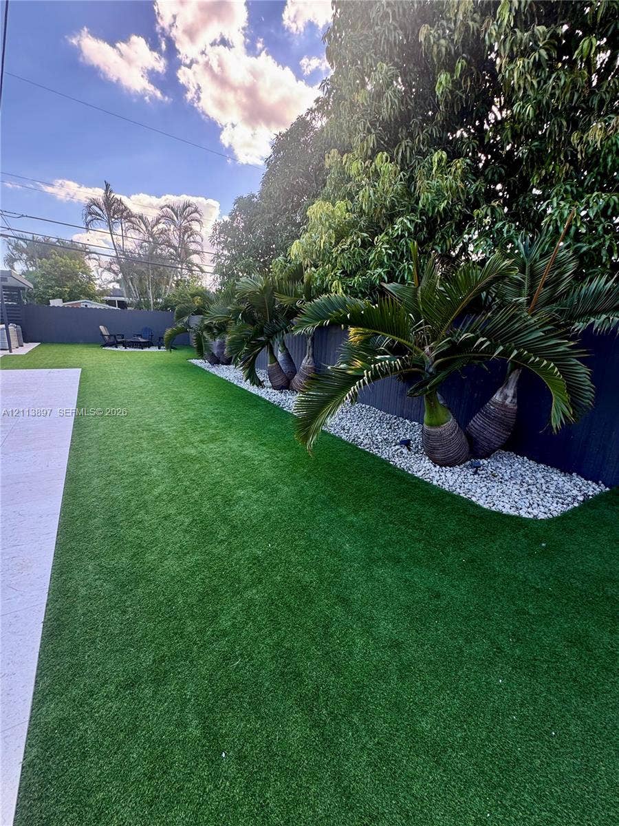 520 E 58th Street, Hialeah, FL 33013 Manicured synthetic lawn, perimeter privacy fencing, and stone-accented landscaping with mature palm trees