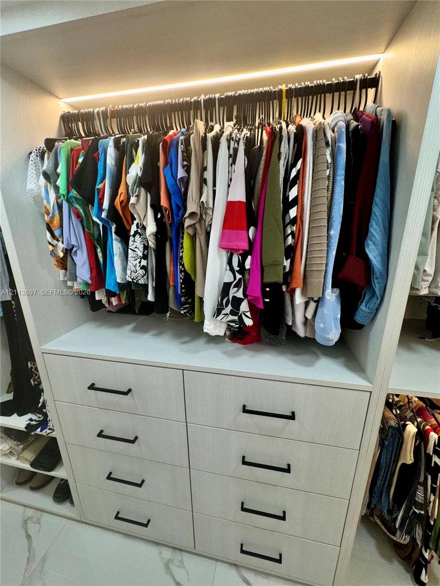 520 E 58th Street, Hialeah, FL 33013 Custom walk-in closet featuring light-toned wood-finish cabinetry, eight soft-close drawers with matte black hardware, integrated linear LED shelf lighting, and stone-look tile flooring