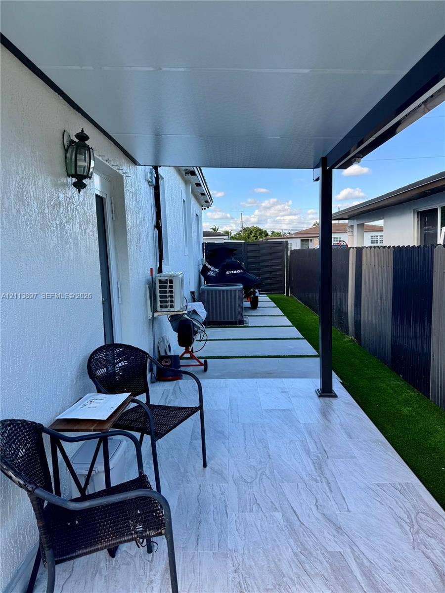 520 E 58th Street, Hialeah, FL 33013 Covered patio featuring large-format porcelain tile flooring, synthetic turf side yard, concrete paver pathway, and wall-mounted exterior lighting