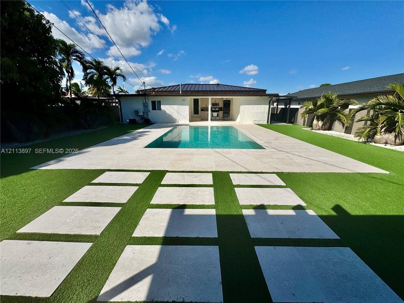 520 E 58th Street, Hialeah, FL 33013 Backyard featuring an inground pool, large stone-finish deck, geometric paver pathway, and synthetic lawn