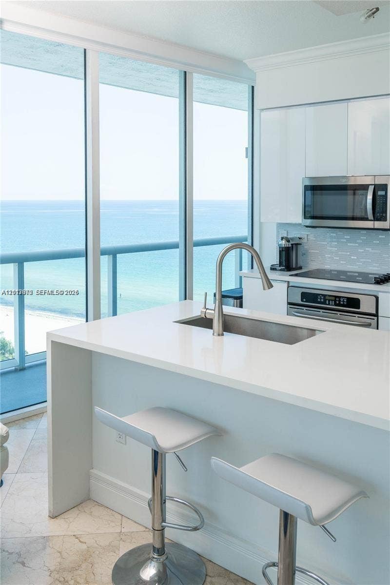 6515 Collins Avenue, #1609, Miami Beach, Miami Beach, FL 33141 Kitchen featuring an eat-in waterfall island, quartz countertops, stainless steel undermount sink, floor-to-ceiling windows, and ocean backdrop