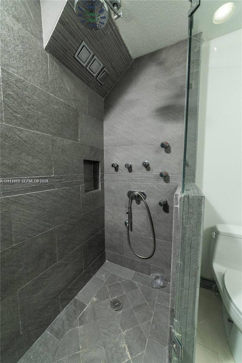 6515 Collins Avenue, #1609, Miami Beach, Miami Beach, FL 33141 Walk-in shower featuring large-format dark grey stone tile walls, a built-in recessed niche, multiple body sprayers, a handheld shower head, and a glass partition