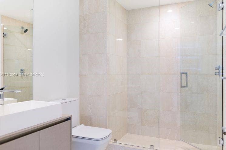 Walk-in shower with floor-to-ceiling neutral tile, frameless glass enclosure, wall-mounted shower head, and built-in vanity with a rectangular basin