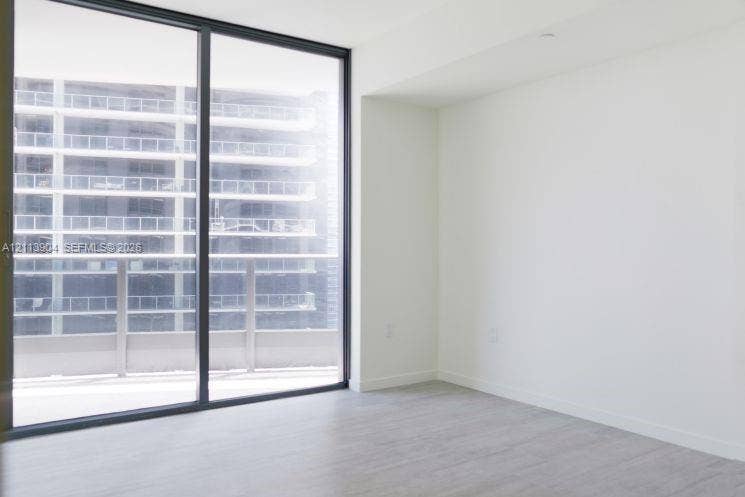 Floor-to-ceiling glass sliding door, neutral wall finishes, wood-finish flooring, and an attached balcony