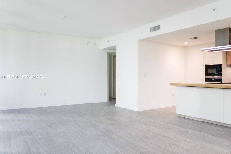 Open-concept interior featuring light wood-finish flooring, white cabinetry, a wood-topped kitchen island, and a stainless steel built-in oven and range hood